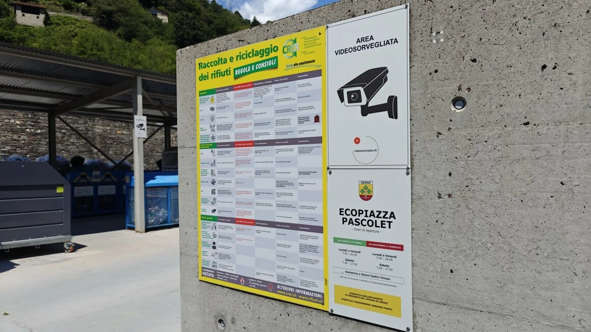 Cartellonistica e videosorveglianza presso Ecopiazza Pascolet Segnaletica di raccolta rifiuti e cartello area videosorvegliata all’ingresso dell’Ecopiazza Pascolet, con contenitori per il riciclaggio sullo sfondo
