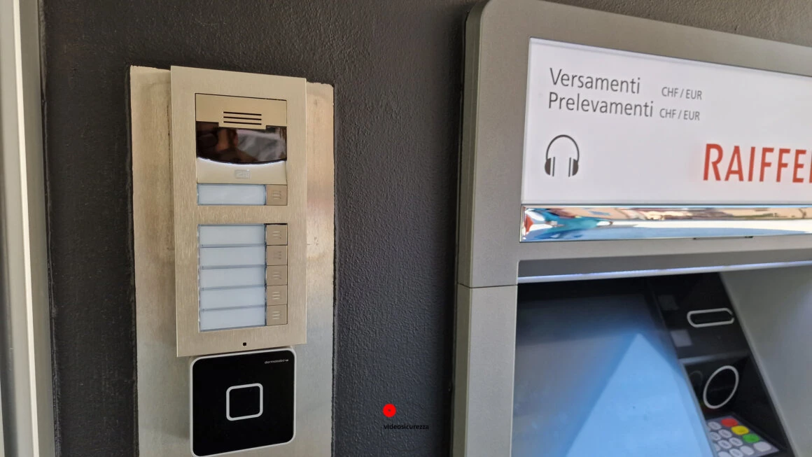 Videocitofono con lettore badge integrato presso sportello bancomat Videocitofono con telecamera e lettore di badge RFID installato a parete accanto a uno sportello bancomat Raiffeisen