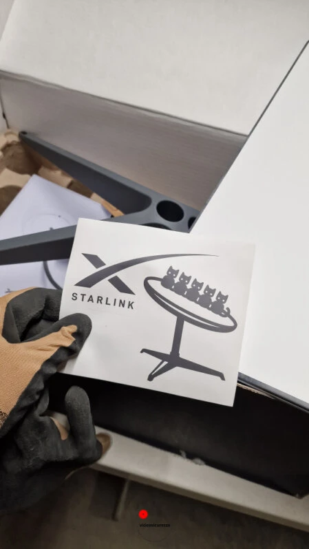 Unboxing kit Starlink con adesivo ufficiale Persona con guanti tiene adesivo Starlink durante apertura del kit di installazione satellitare