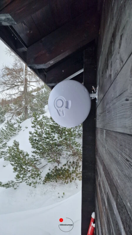 Access point Wi-Fi installato all’esterno in ambiente innevato Access point wireless montato su parete in legno di baita alpina, con sfondo innevato e alberi in ambiente montano