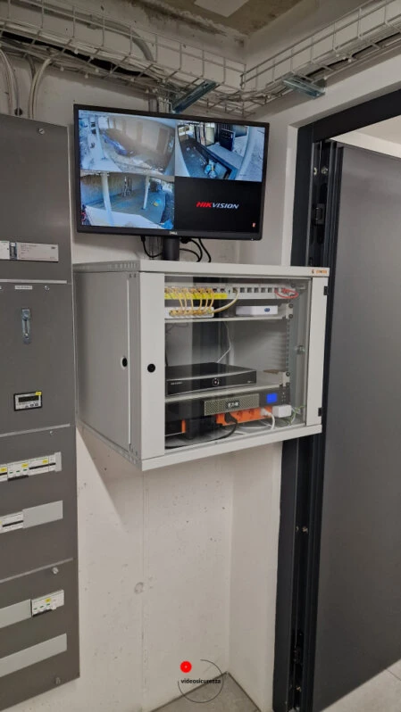 Armadio di rete con NVR e monitor per videosorveglianza interna Armadio rack a muro contenente registratore NVR e router, con monitor che mostra le riprese delle telecamere di videosorveglianza interne