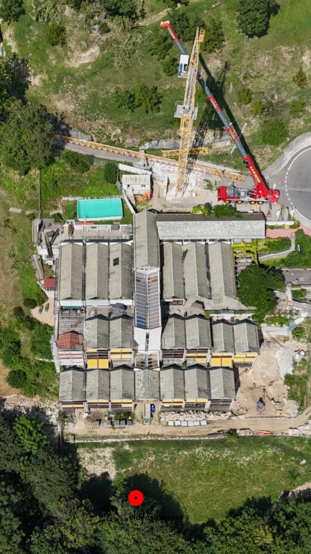 Ripresa aerea verticale di cantiere e edificio industriale Immagine aerea scattata con drone che mostra un grande edificio industriale con gru e mezzi da cantiere durante lavori di ristrutturazione