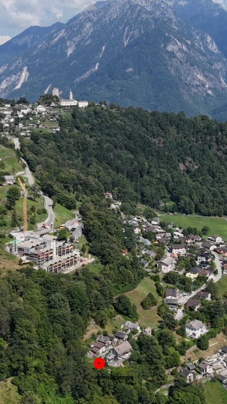 Ripresa aerea panoramica di borgo montano e area residenziale Vista aerea con drone di un centro abitato in area montana, con case immerse nel verde e panorama alpino sullo sfondo