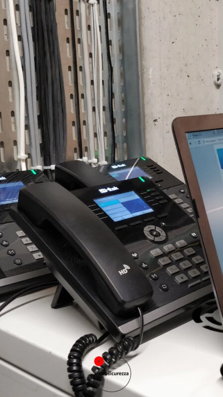 Telefoni VoIP professionali in fase di configurazione tecnica Telefoni VoIP da scrivania in configurazione su banco tecnico con notebook, cablaggio visibile sullo sfondo